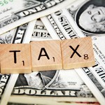 on top of a pile of cash, scrabble tiles spell out T-A-X